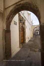 Image du Maroc Professionnelle de  Dans une rue des Habous, la succession des balèvres, moulure, arches, portiques et autres éléments décoratifs, projetent les visiteurs dans l’ardeur avec un élan de force et de fierté d’une époque révolue. Conçu par les architectes Auguste Cadet et Edmond Brion d’après l’ébauche d’un premier plan-masse dû à Albert Laprade, le quartier fait partie des endroits les plus pittoresques de Casablanca, il fut La construction n’avait commencé qu’après la première guerre mondiale. Situé près du Palais Royale, ce joyau architectural fait partie du patrimoine architectural de la ville, Samedi 8 Novembre 2008. Au centre le minaret de La mosquée Ben Youssef. (Photo / Abdeljalil Bounhar)
